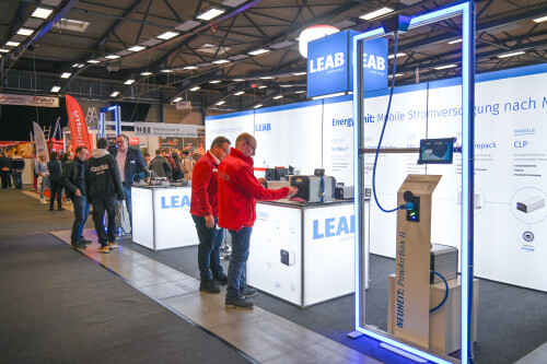 Beleuchteter Messestand von LEAB mit Besuchenden.