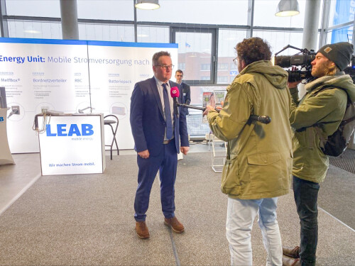 A man speaks into a microphone of the TV channel SAT.1 in front of the LEAB stand.