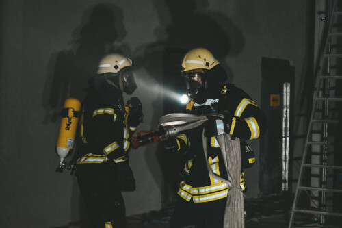 Two firefighters carry a hose in the dark