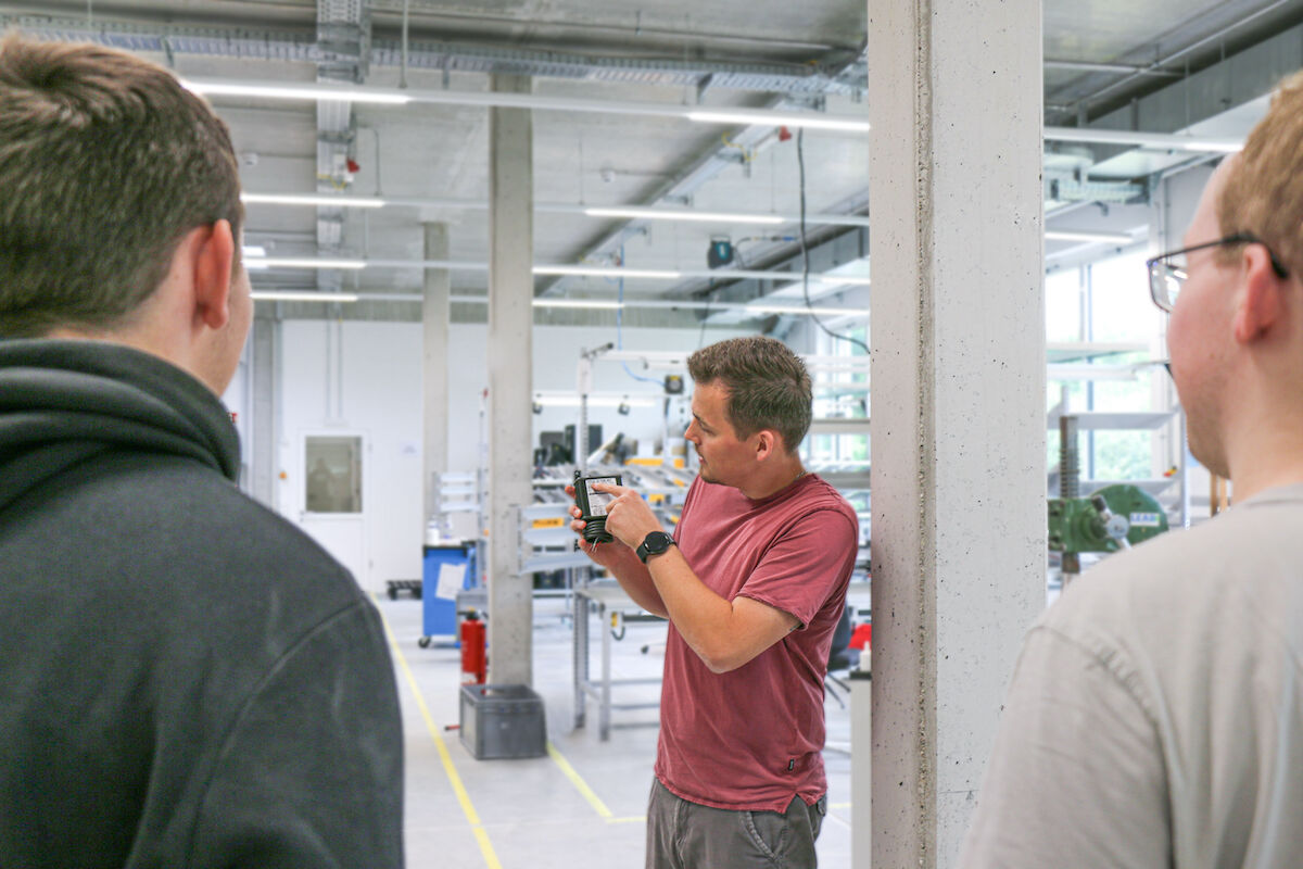 Produktionsleiter Finn Krüger zeigt auf ein Gerät in seiner Hand