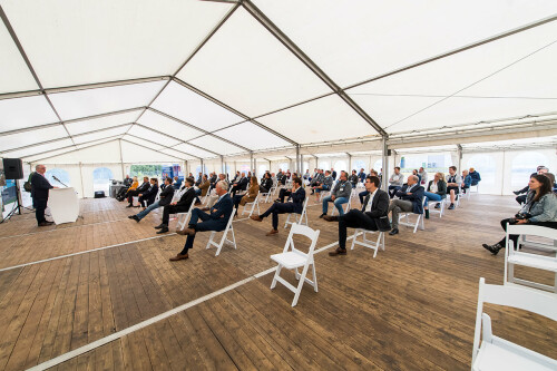 Guests sit on white chairs with a lot of distance during a speech