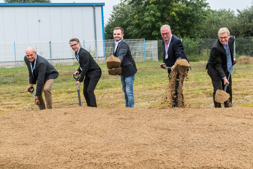 Five men in suits laughingly shovel sand