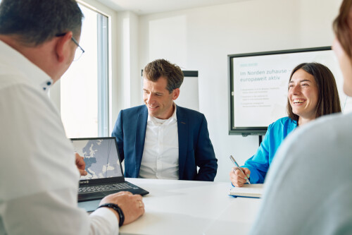 Two men and two women at a desk with an open laptop.