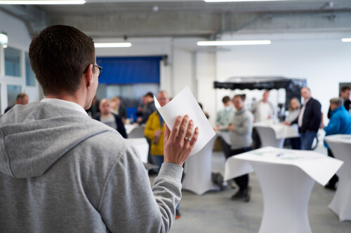 A person with a piece of paper in his hand stands in front of a blurred crowd.